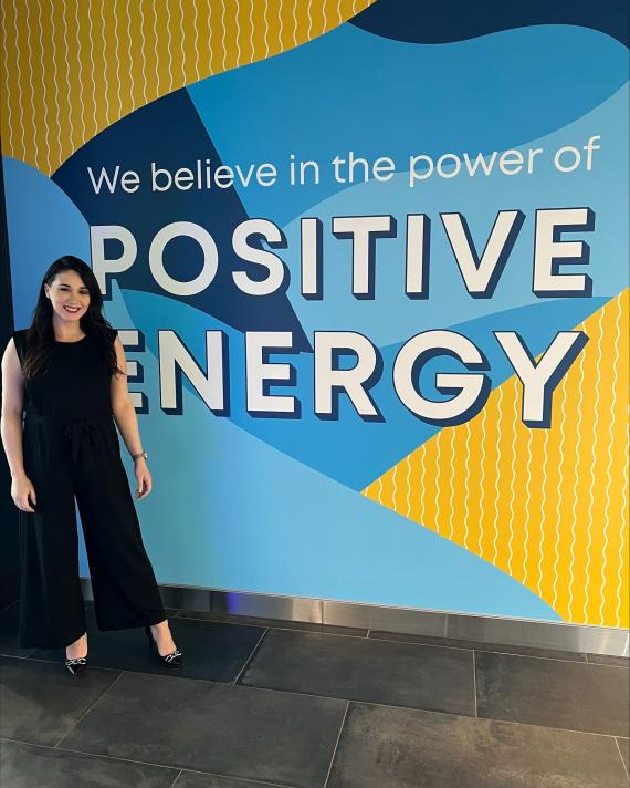 NFE Employee standing by sign reading "we believe in the power of positive energy"